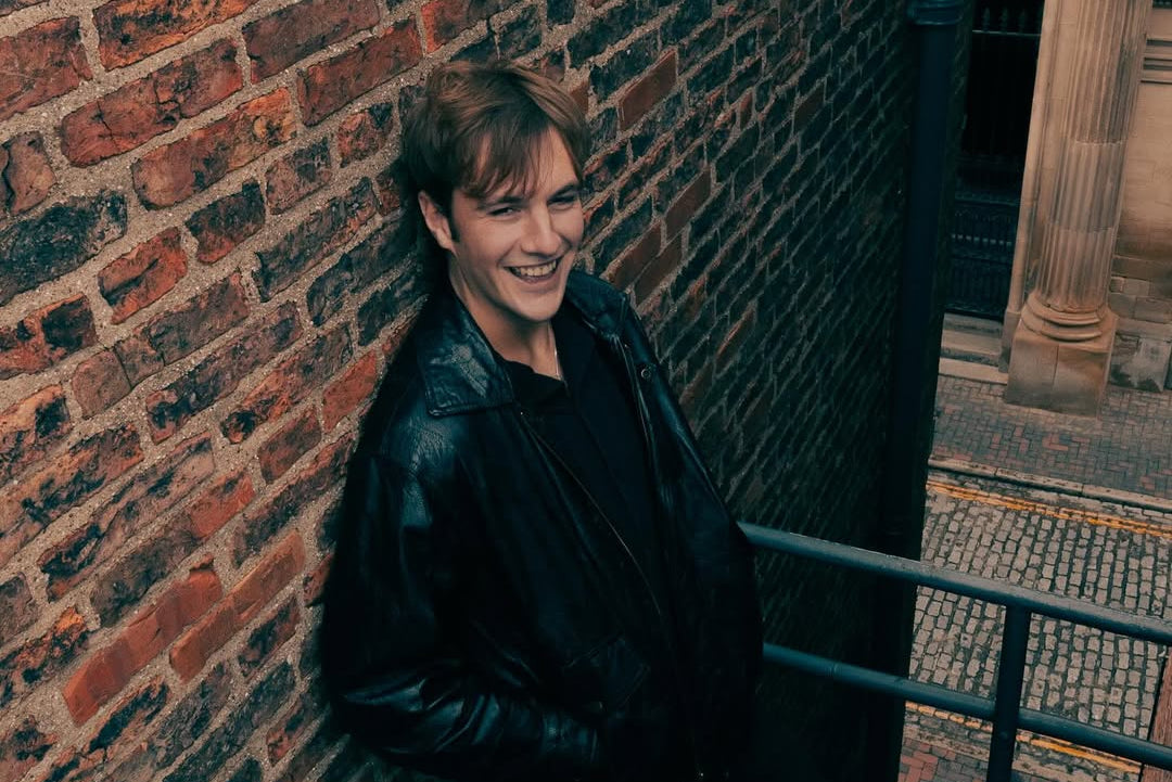 Person leaning against a brick wall with a smile